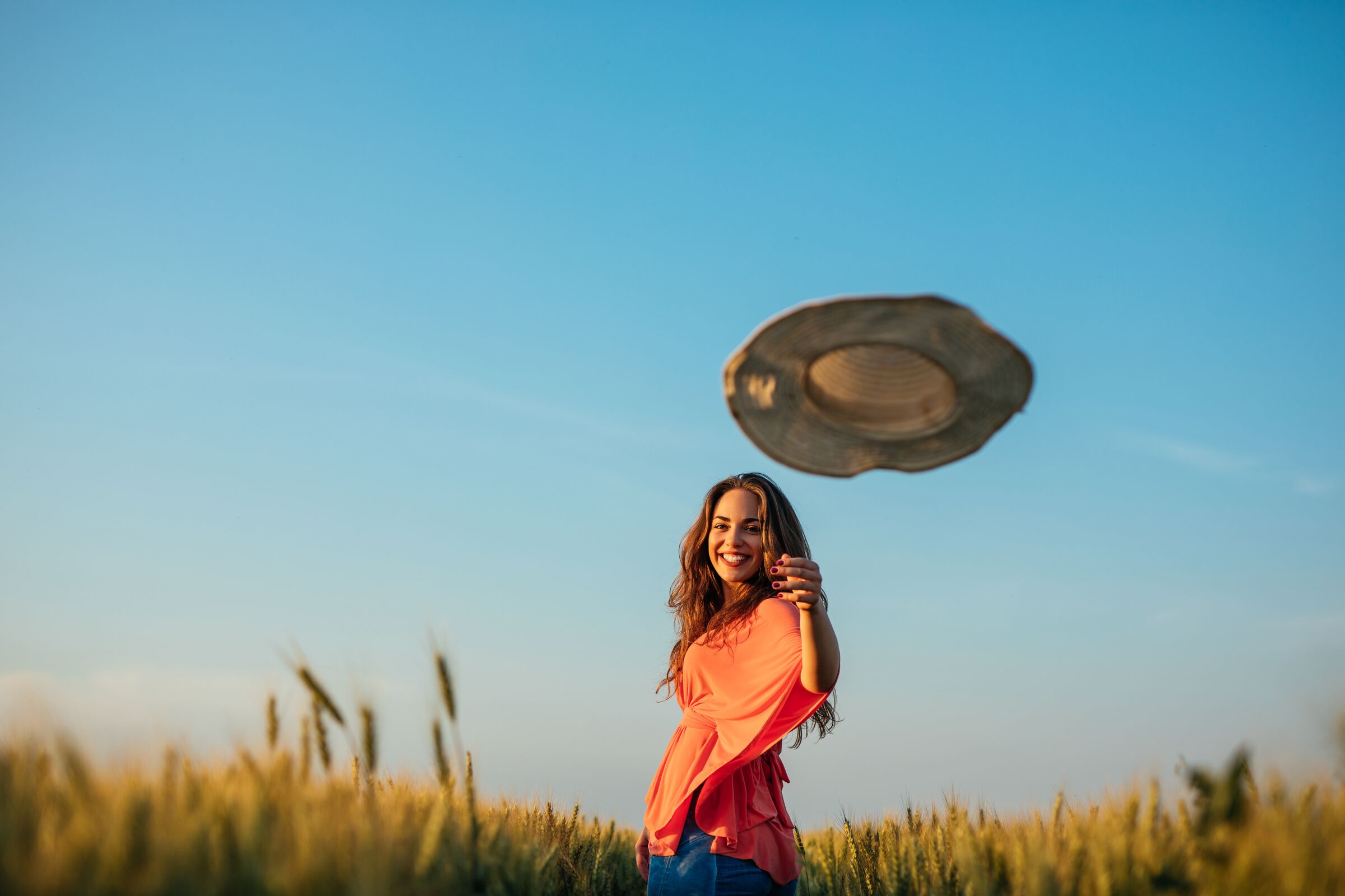 Smiling woman tossing her sun hat in a golden wheat field
